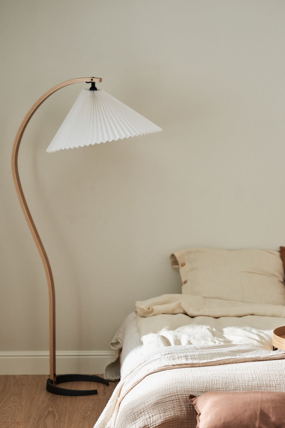 Renueva tu hogar con estas ideas modernas de iluminación. Aquí ves la lámpara de pie Gubi Timberline con su pata de madera curvada, colocada junto a una cama.