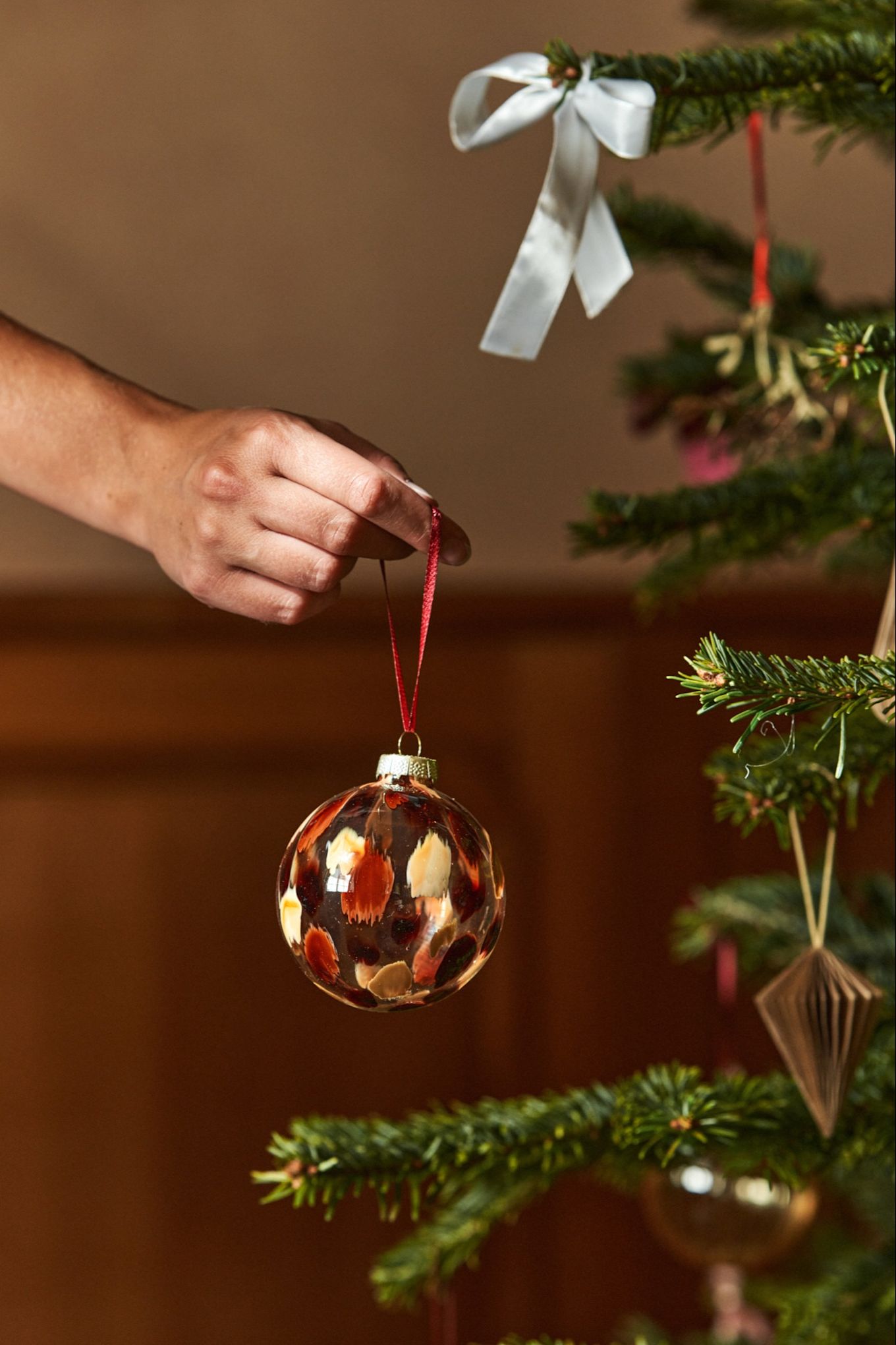 Una mano cuelga una bola de vidrio en un árbol. Las decoraciones de vidrio son siempre tendencia, y no iba a ser menos en la Navidad de 2024.