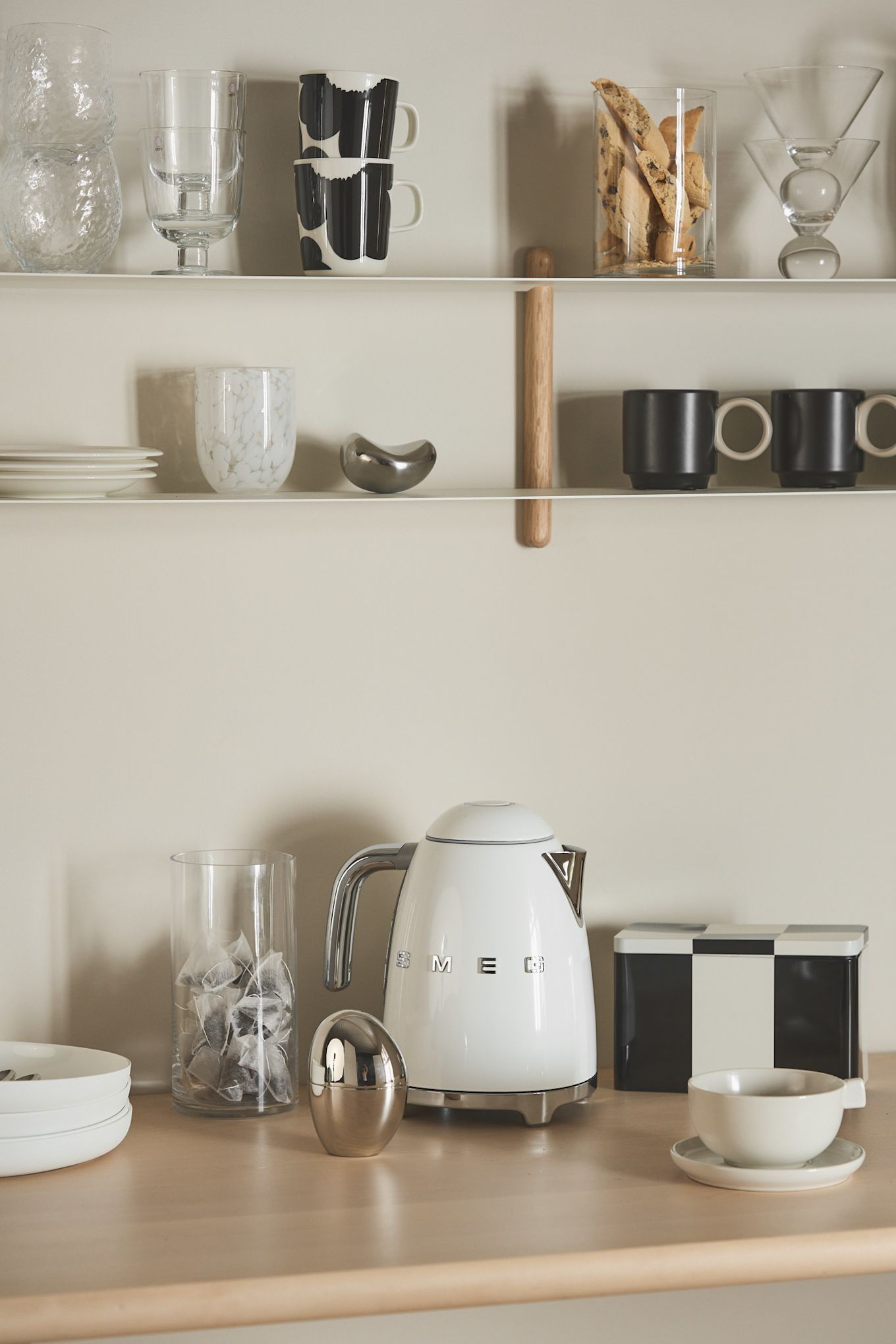 Ten un hervidor a mano en tu rincón del café, como este de Smeg, que se encuentra aquí en un rincón del café, rodeado de una estantería con varias tazas y cajas.