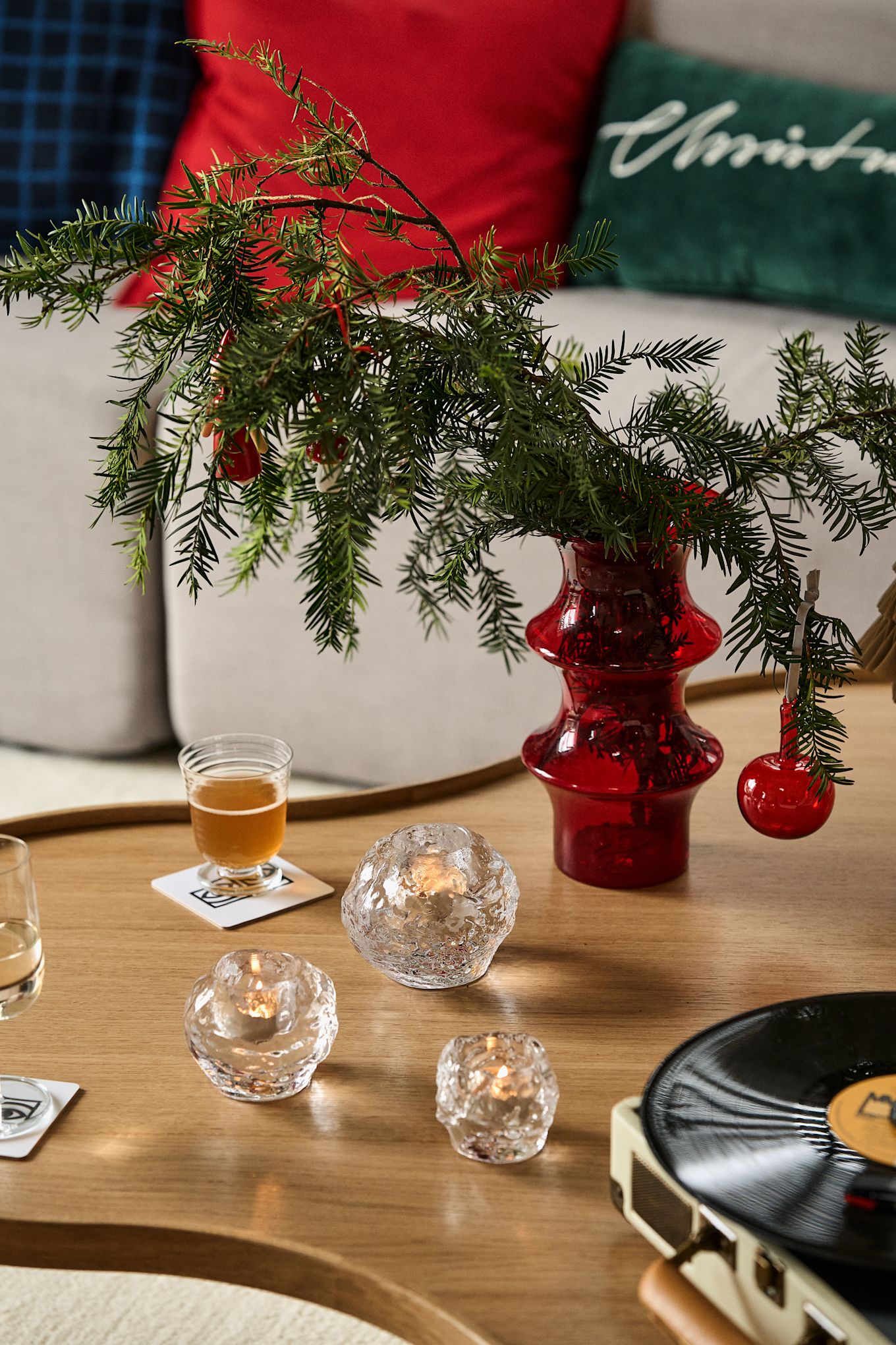 Ideas de regalos para Navidad: Aquí se ve una mesa de madera con un jarrón y ramas de abeto dentro, y delante de él, tres portavelas de la colección Snowball de Kosta Boda.