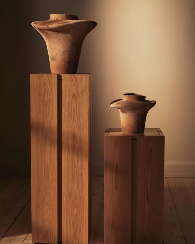 Dos jarrones de cerámica terrosos y acampanados sobre pedestales de madera clara.