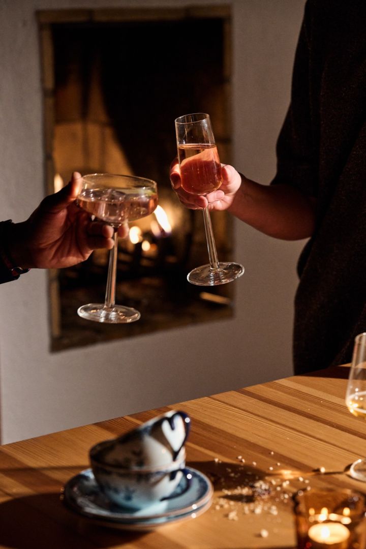 Manos brindan con dos copas Essence de Iittala frente a una chimenea durante una celebración navideña nórdica.