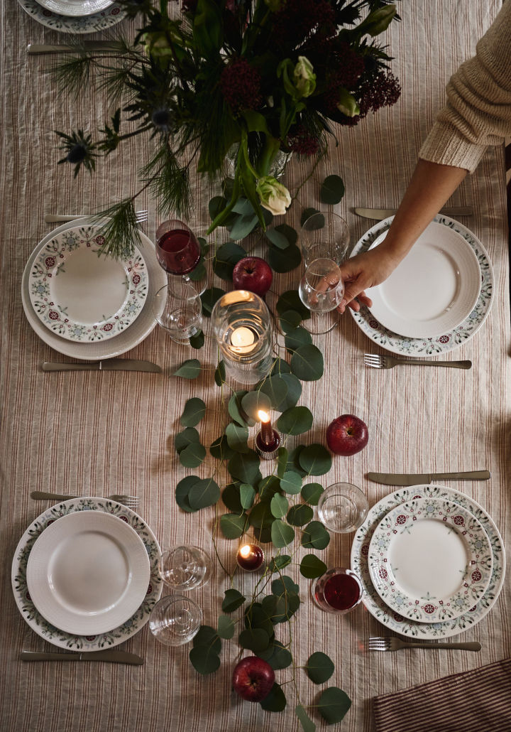 Una idea sencilla y elegante para poner la mesa en Navidad, fotografiada desde arriba con hojas verdes y manzanas rojas como decoración.