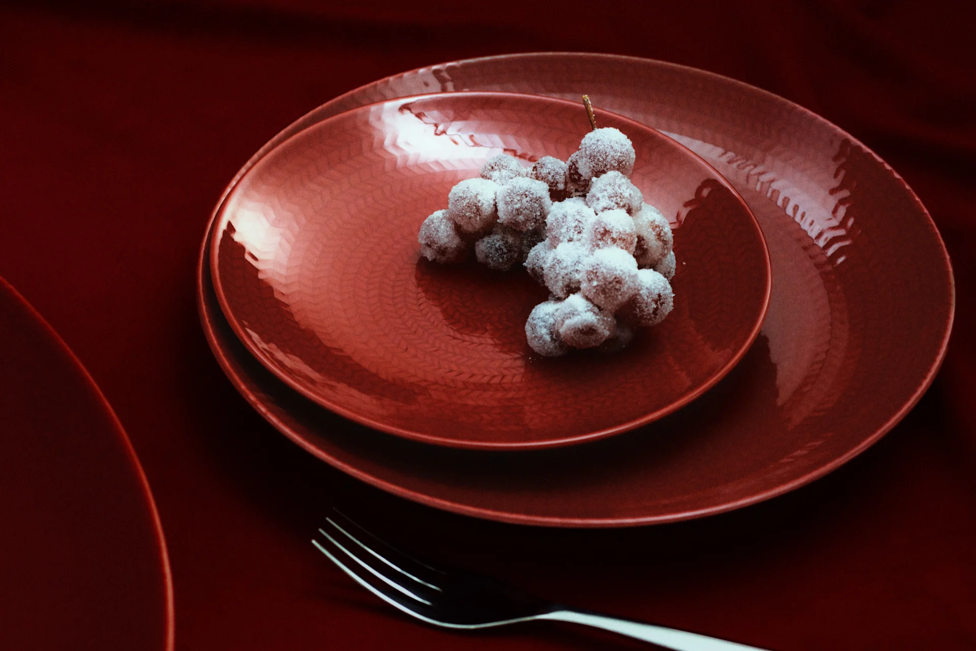 Uvas azucaradas en platos rojos texturizados con tenedores sobre un mantel rojo oscuro.