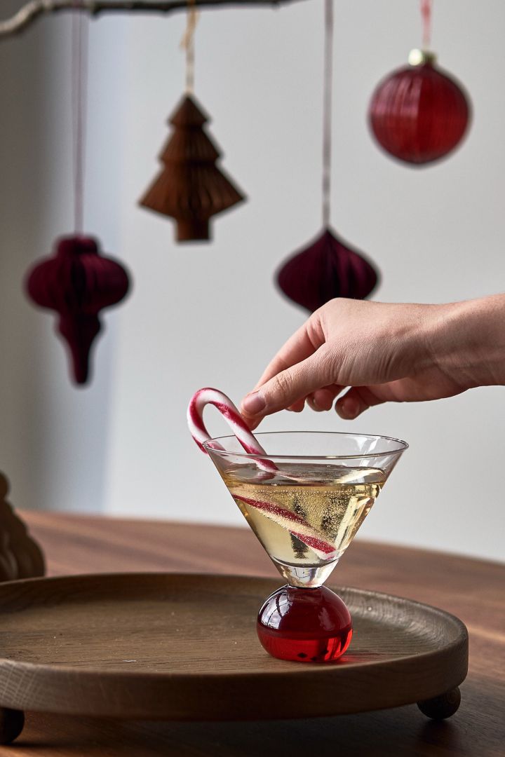 Servir un cóctel navideño sencillo con glögg y burbujas en un vaso Spice de Byon, decorado con una caña de caramelo.