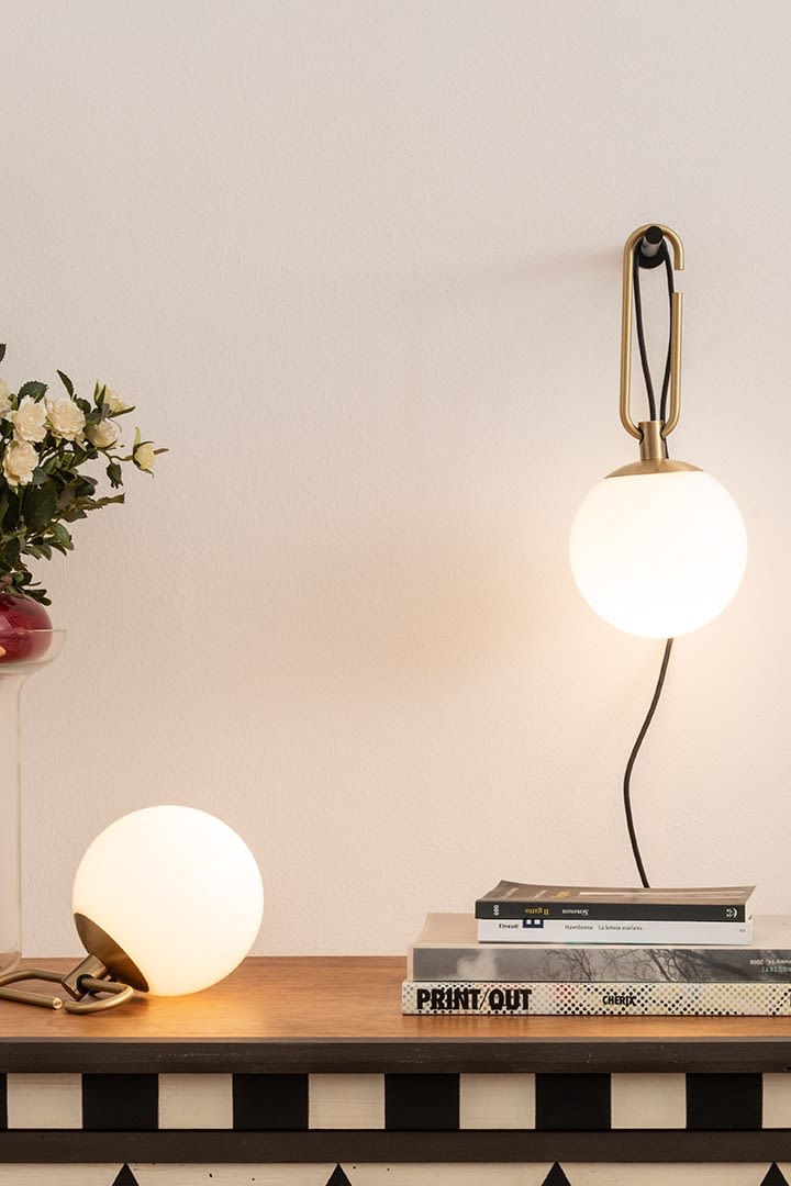 Las lámparas de pared y sobremesa NH de Artemide cuelgan y se sostienen sobre un escritorio con una pila de libros.