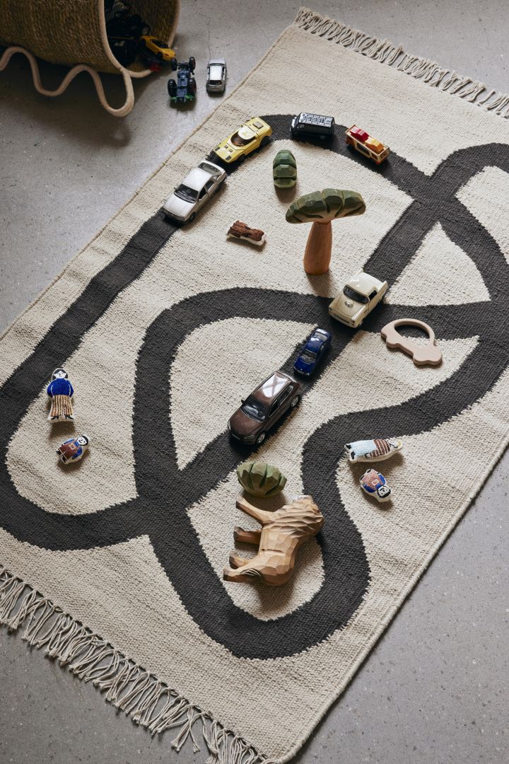 Una alfombra suave y agradable para jugar es imprescindible a la hora de decorar la habitación infantil. Aquí la alfombra Lane de Ferm Living en color beige con estampado negro que puede actuar como pista o camino para coches y figuras.