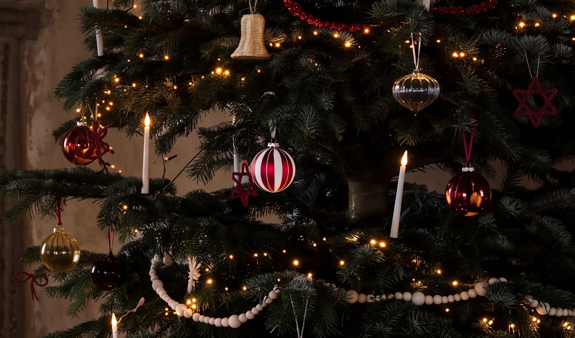 Un árbol de Navidad decorado con luces cálidas, bolas rojas, plateadas y doradas, velas blancas y guirnaldas de cuentas de madera.