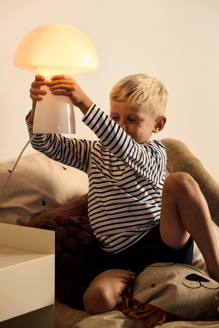 Aquí ves a un niño sosteniendo la lámpara de mesa en forma de seta Fungo de Globen Lighting.