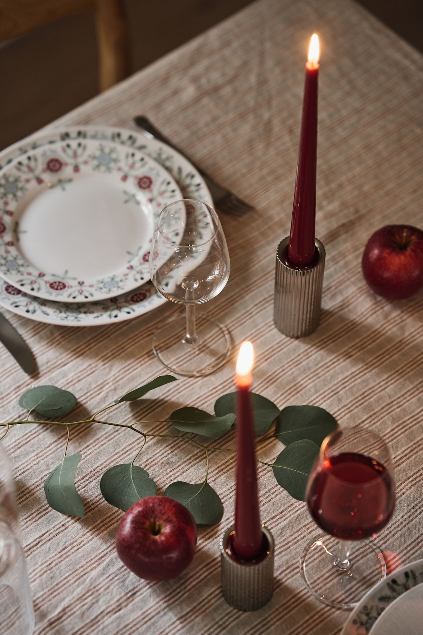 Primer plano de velas de color rojo intenso en portavelas cromados como parte de una sencilla mesa navideña.