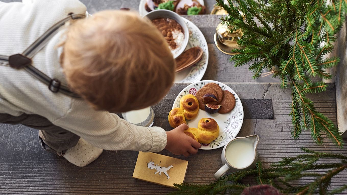 Aquí puedes ver a un niño alcanzando un lussekatt en un plato de la colección Swedish Grace Winter de Rörstrand.