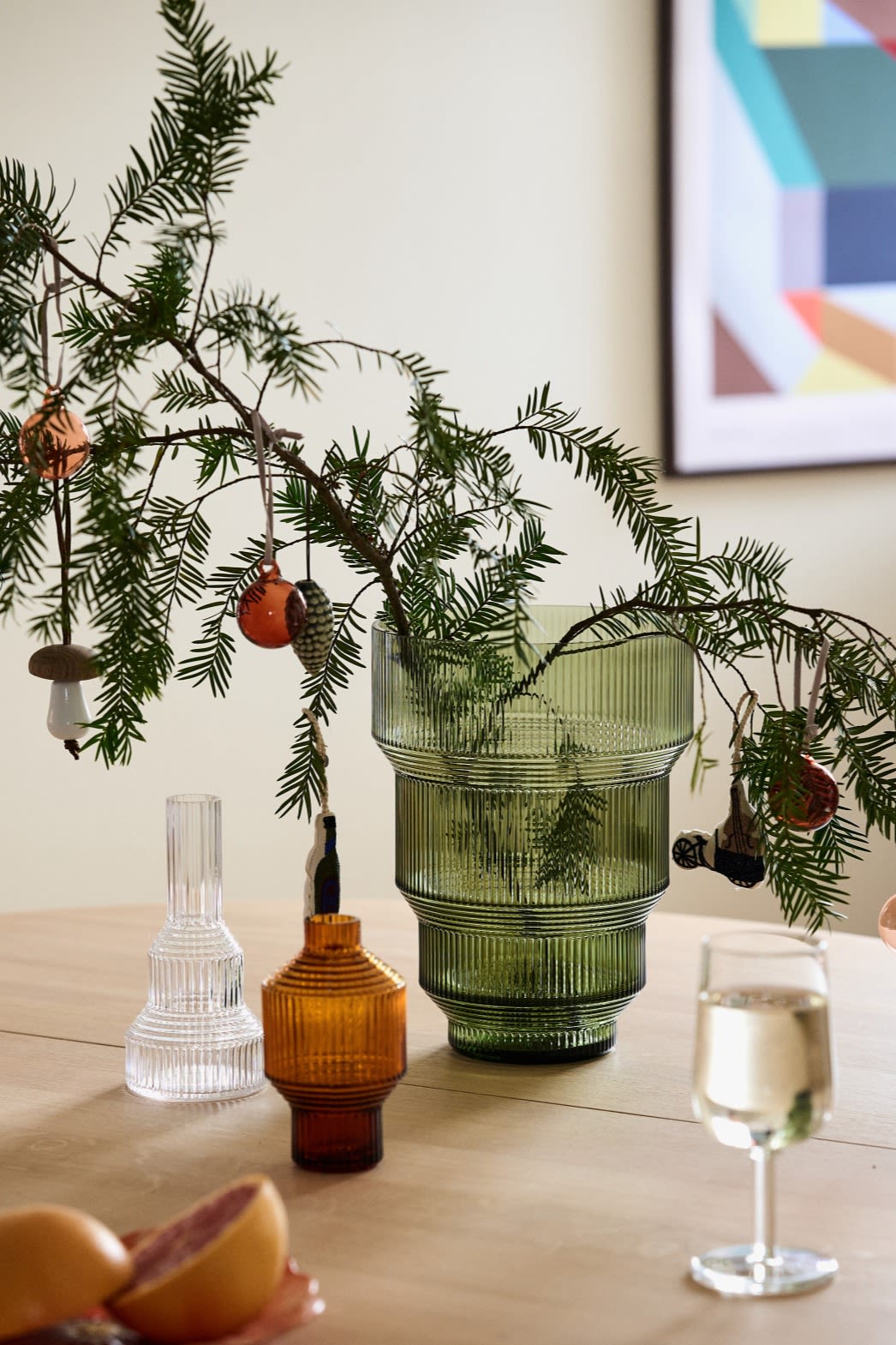 Manualidades navideñas con ramas de abeto: aquí se ven ramas de abeto en el jarrón verde Pavillon de Kosta Boda, decoradas con bolas de Navidad, sobre una mesa.