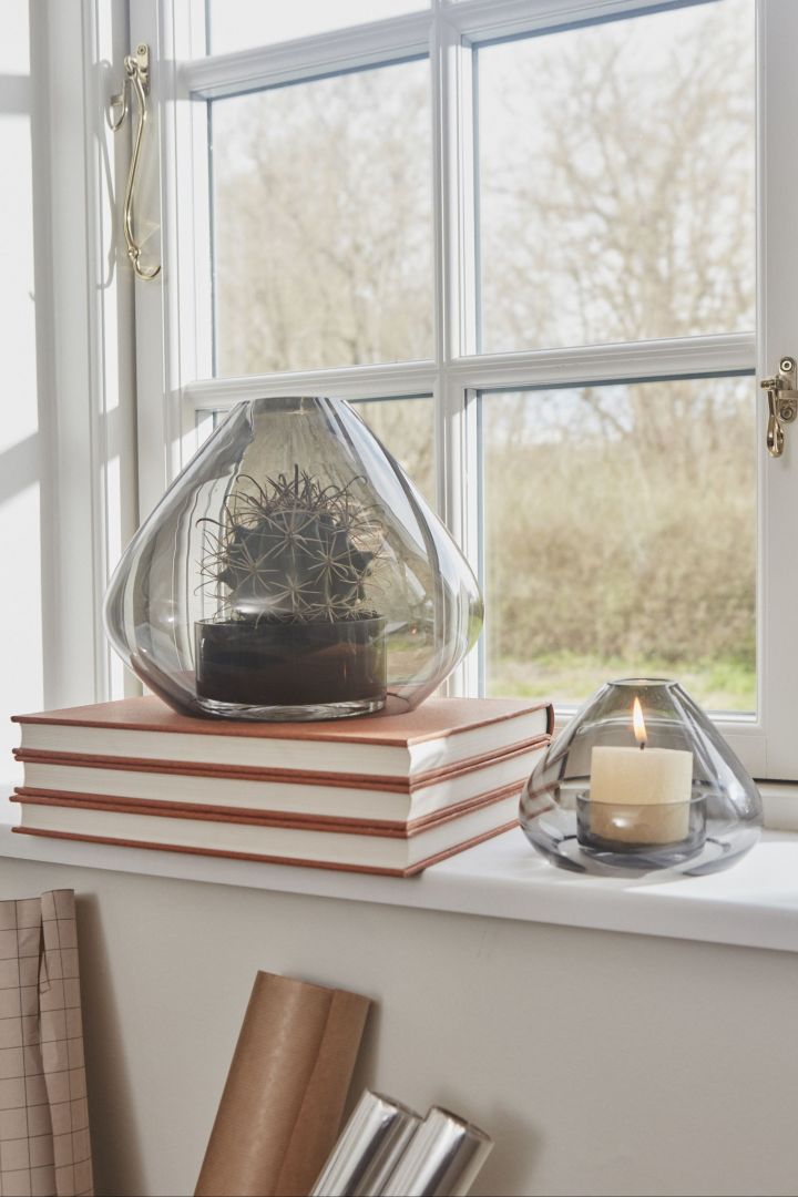 Aquí puedes ver la linterna Uno de AYTM en dos tamaños diferentes en el alféizar de una ventana.  El grande se ha colocado sobre una pila de libros y contiene un cactus; el pequeño, una vela.