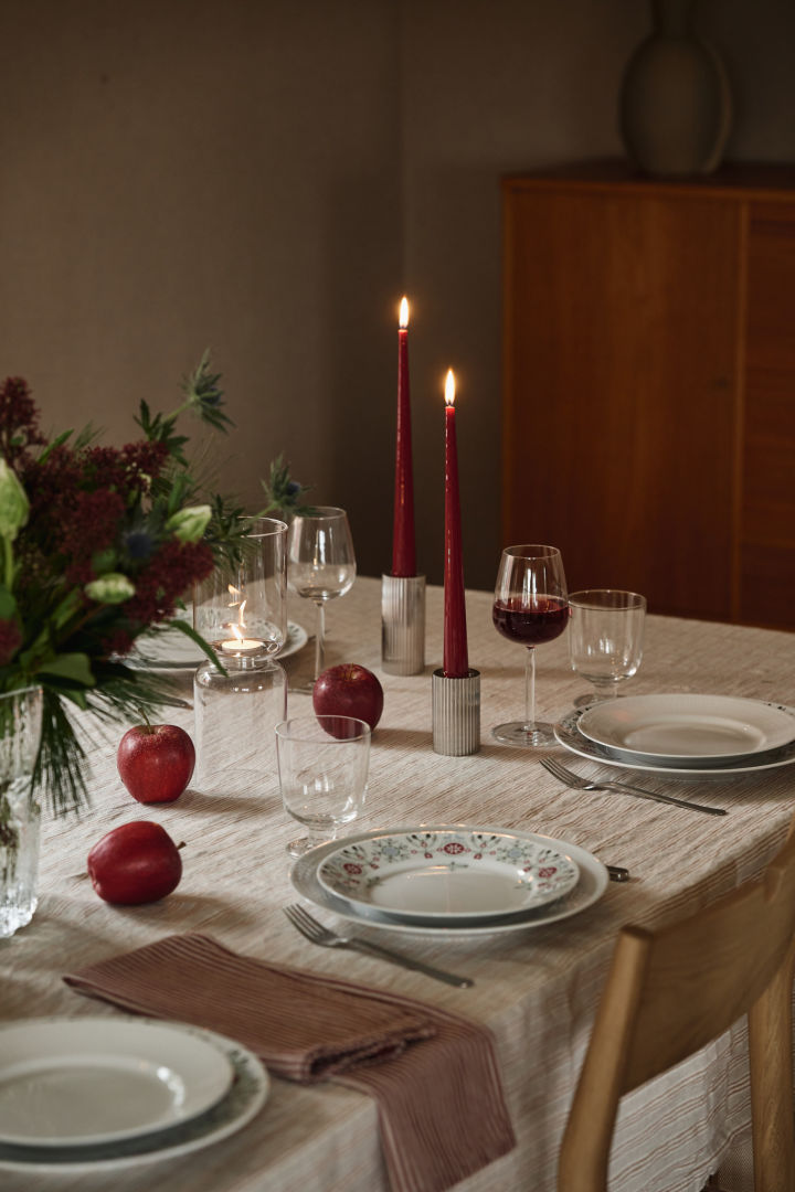 Velas rojas de Navidad sobre una sencilla mesa navideña con platos estampados y detalles rojos.