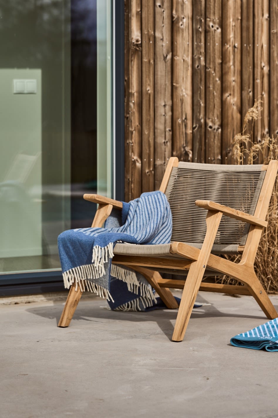 Una terraza escandinava con la silla lounge Sandvik de 1898 y la manta de lana Stripes azul de NJRD.