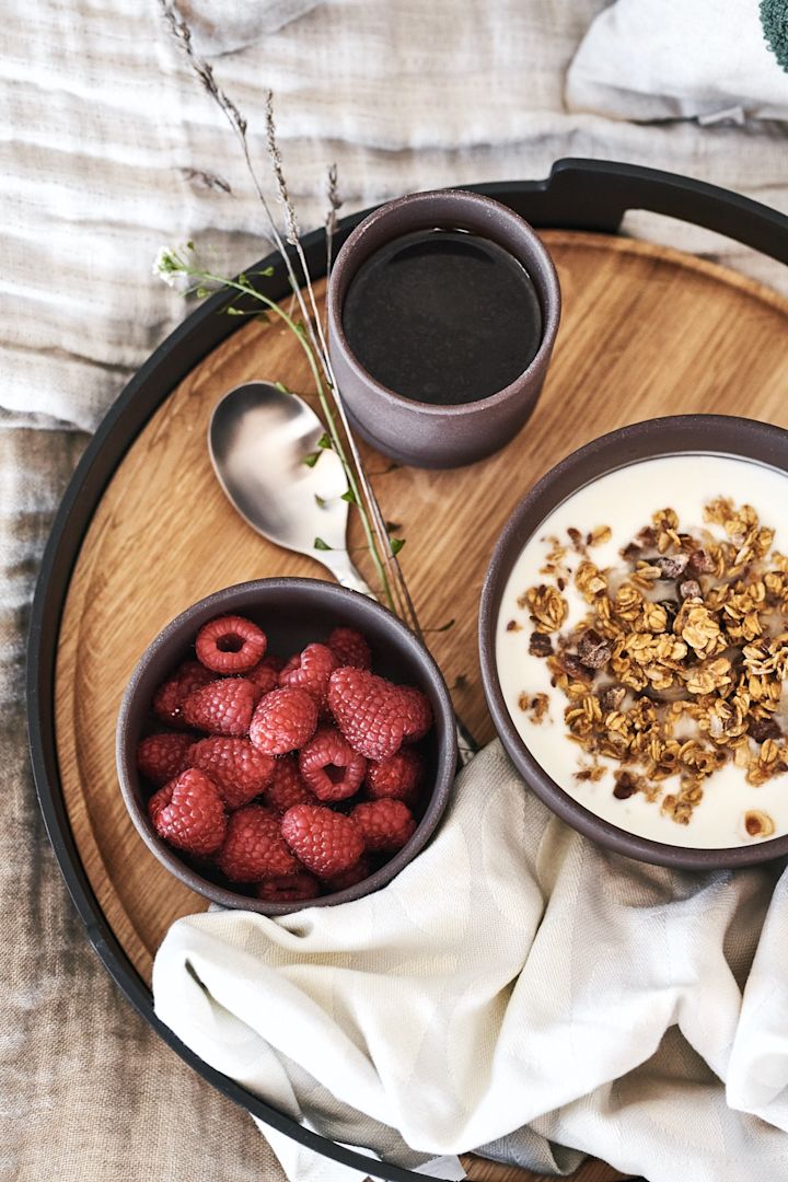 Un desayuno de lujo en la cama servido en una preciosa bandeja de Eva Solo con bayas y muesli en cuencos marrones de Ferm Living.