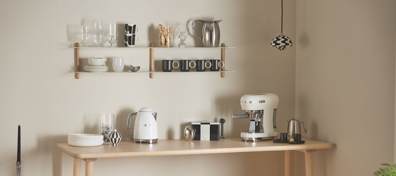 Aquí puedes ver un rincón del café bien organizada con una cafetera y un hervidor de Smeg, tazas y recipientes de café, así como una lámpara colgante Flowerpot de &tradition.