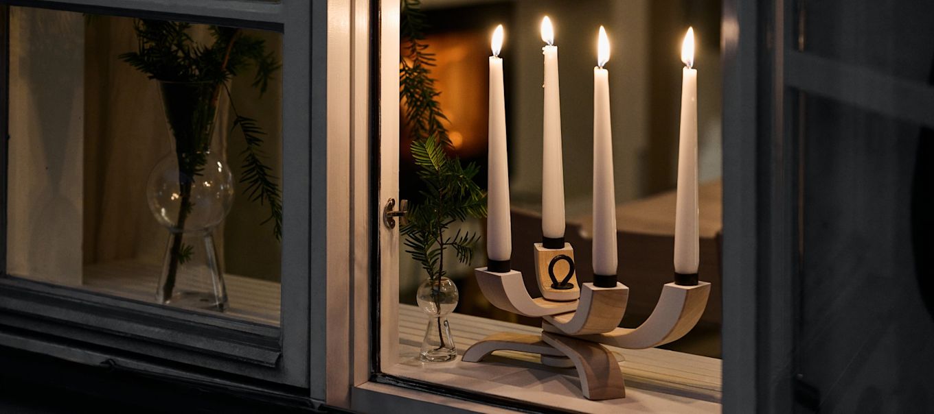 Un típico portavelas escandinavo, como el portavelas Nordic Light de Design House Stockholm, que se muestra aquí en una ventana abierta, es imprescindible en todas las Navidades suecas y suele formar parte importante de las historias navideñas escandinavas.