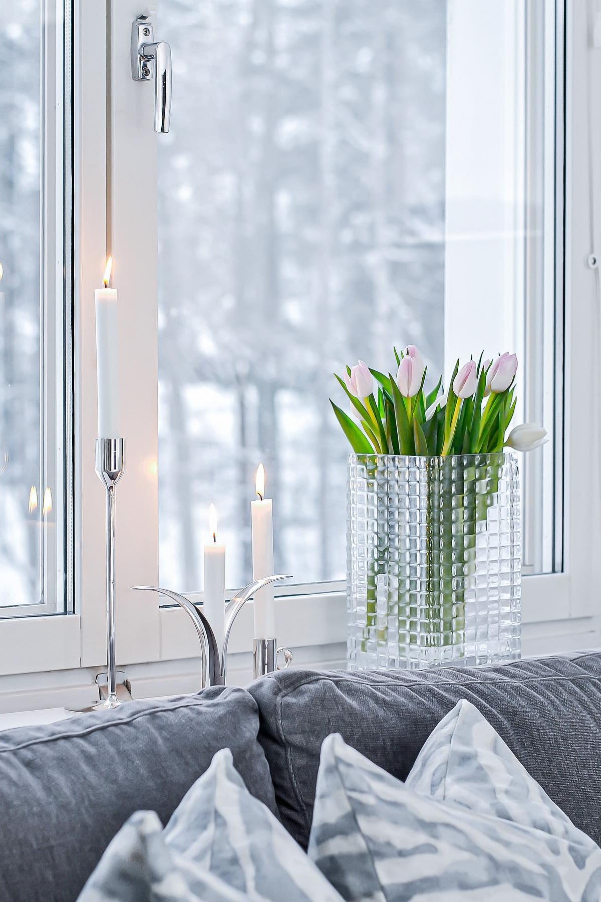 Decora el alféizar de tu ventana con velas o flores bonitas, sobre todo en los meses más oscuros. Aquí puedes ver tulipanes frescos en el jarrón City Hurricane de Louise Roe, junto a varios candelabros plateados con velas blancas en ellos en el alféizar de @josefinsinredning.