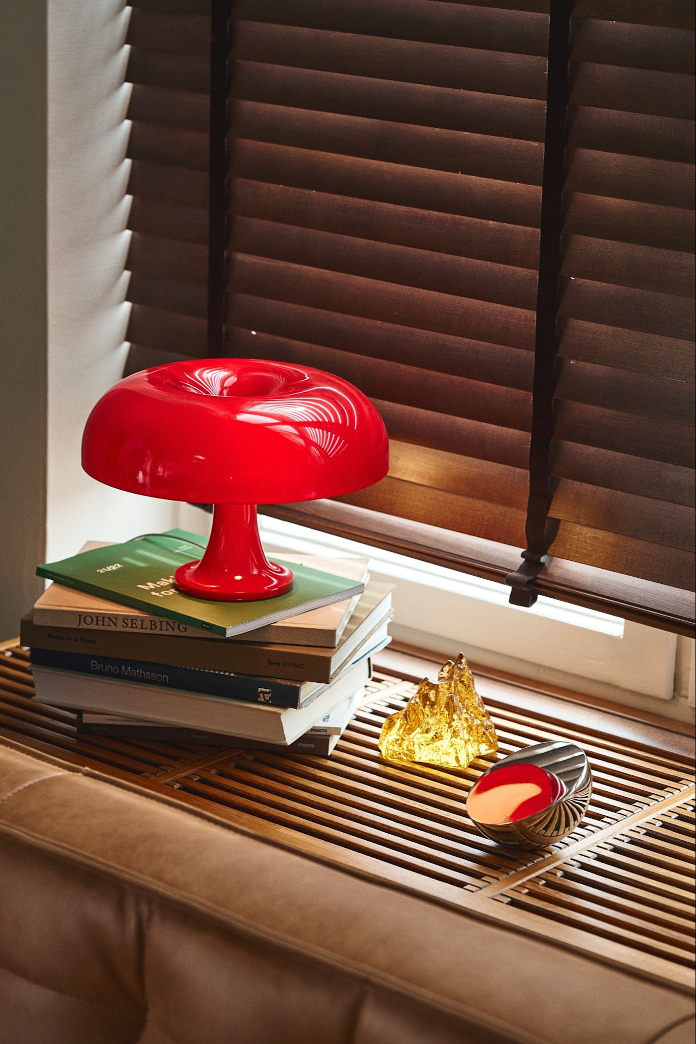 Aquí vemos una de las lámparas más populares del otoño y que sigue la tendencia retro predominante: la lámpara de mesa Nessino en rojo brillante encima de una pila de libros en un alféizar de madera oscura de estilo retro.