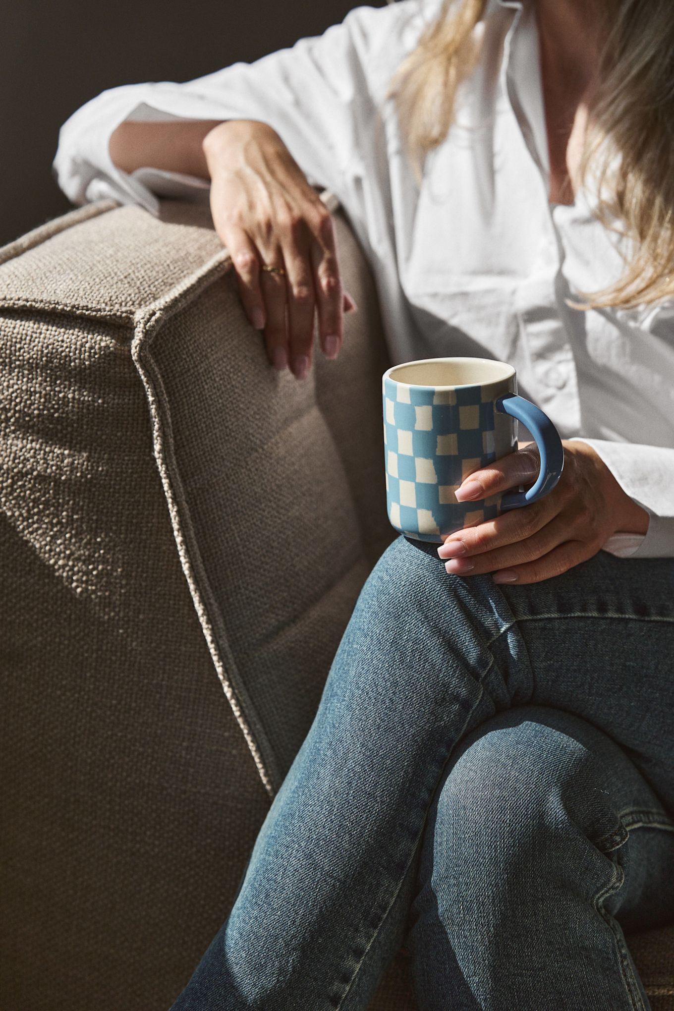 Los cuadros y las rayas son una de las grandes tendencias según las tendencias de diseño de interiores de otoño de 2024. Aquí se ve a una mujer sentada en un sillón sosteniendo una taza de cuadros azules de Byon.