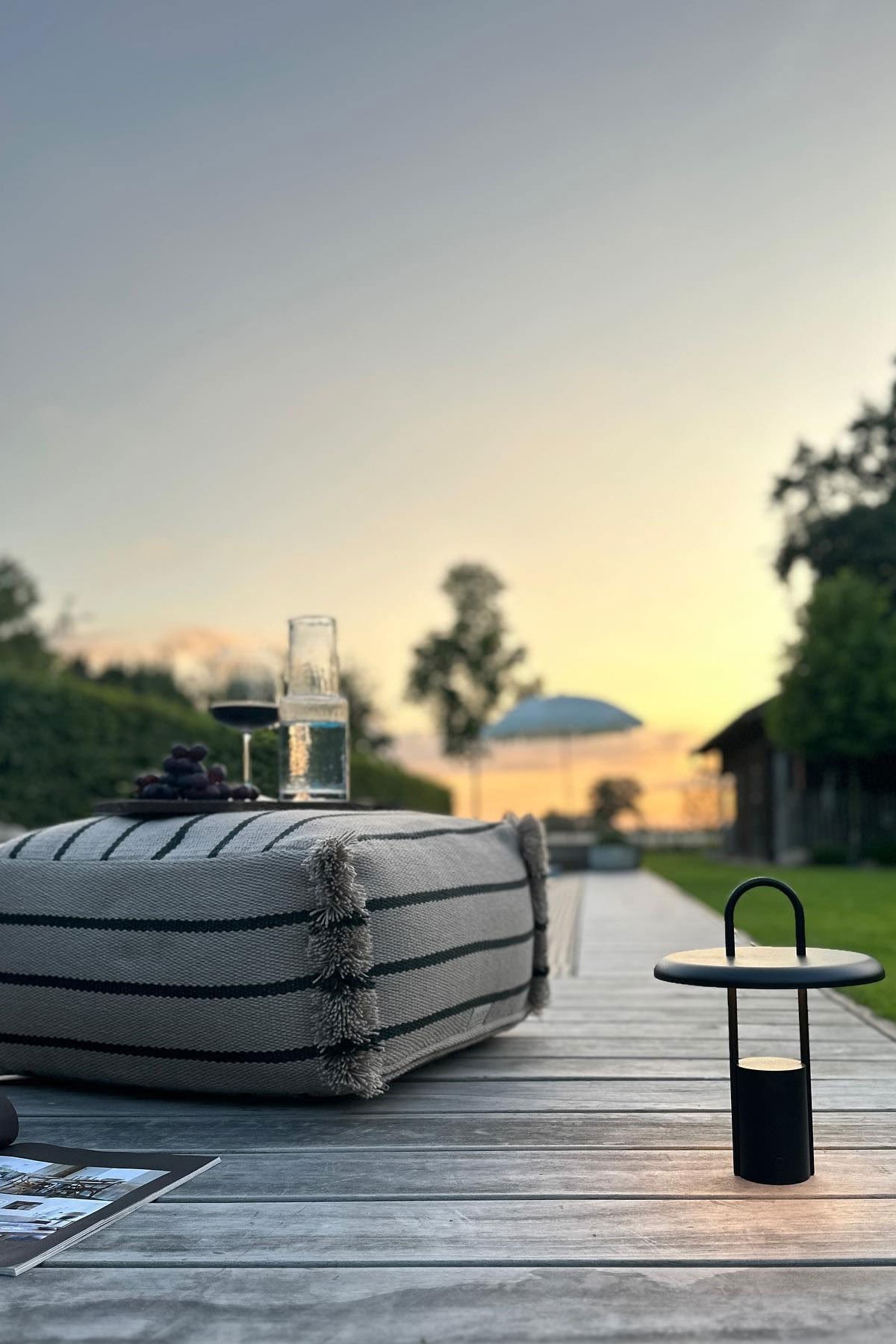 Una terraza acogedora con suelo de madera, cojín para sentarse Lina de OYOY y lámpara de mesa Pier negra de Stelton.