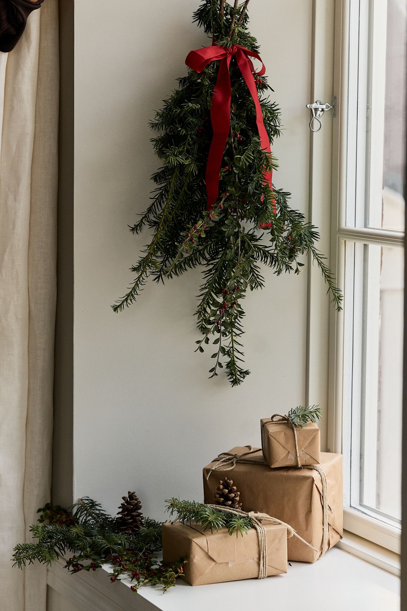 Manualidades navideñas con ramas de abeto: aquí se ve un ramo de ramas de abeto colgado en una ventana, con algunos regalos pequeños sobre el alféizar debajo.