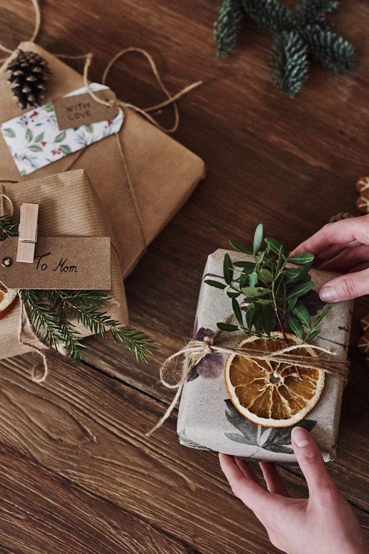 Regalos de Navidad envueltos en papel de tapiz, decorados con rodajas de naranja seca y ramitas de pino.