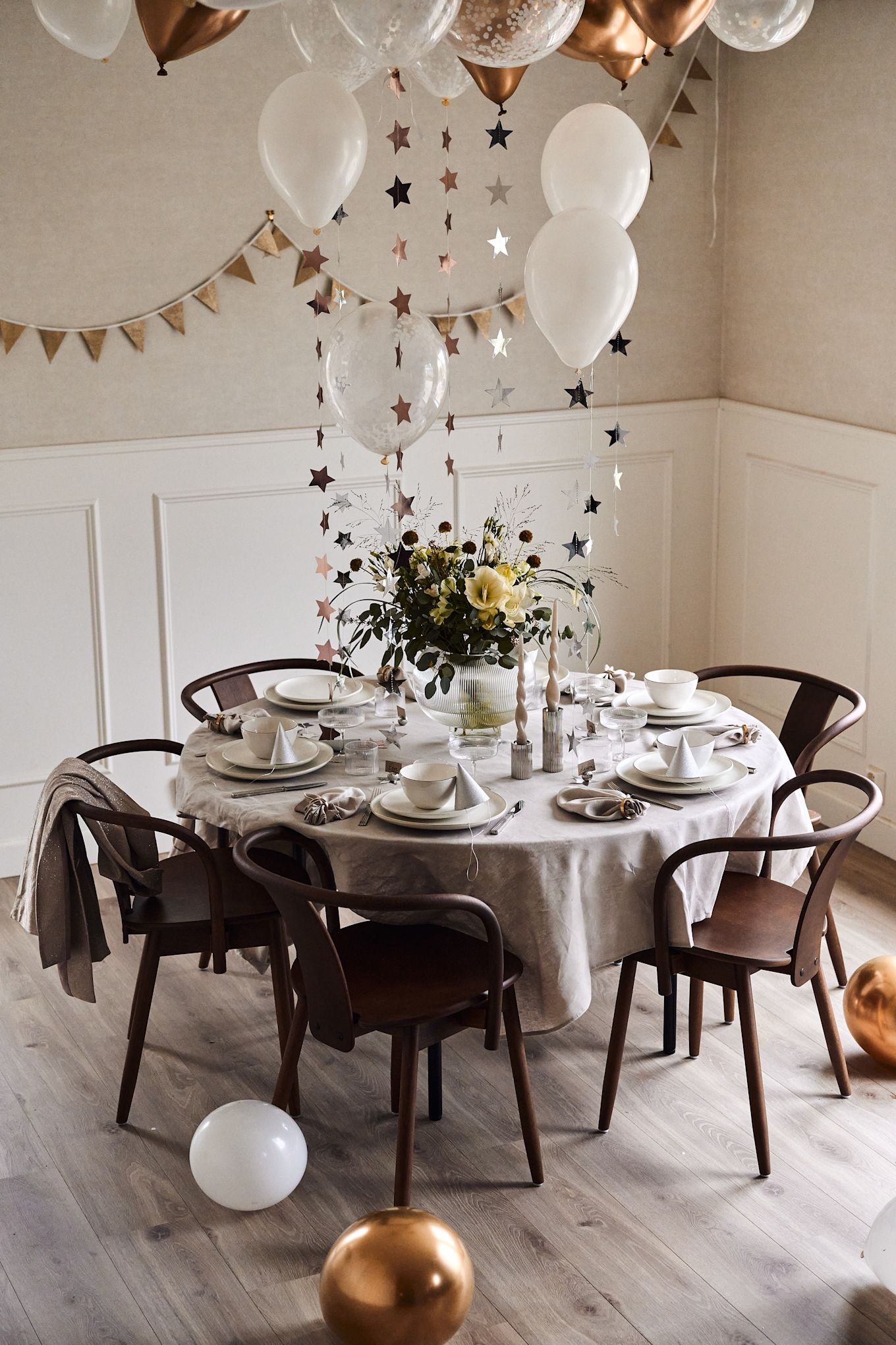 Ideas para fiestas de fin de año: decora la mesa con globos y estrellas colgantes en una sencilla combinación de colores en blanco y dorado.