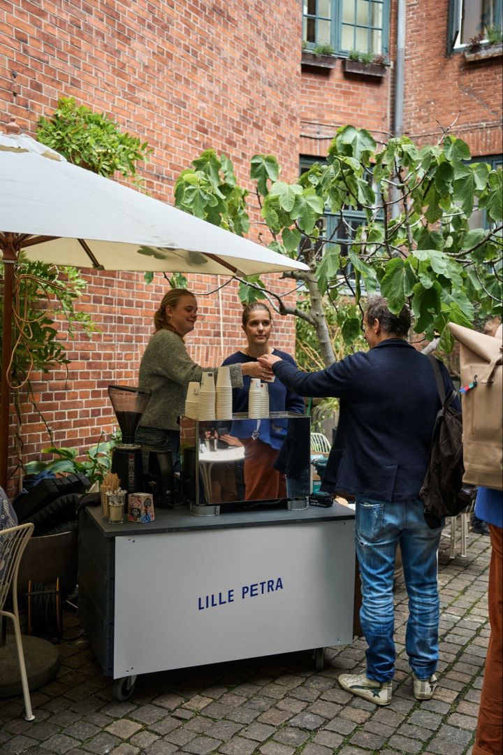 Haz una parada en el Café Lille Petra durante tu visita a Copenhague para amantes del diseño. Aquí puedes ver al personal ofreciendo café en el patio. 