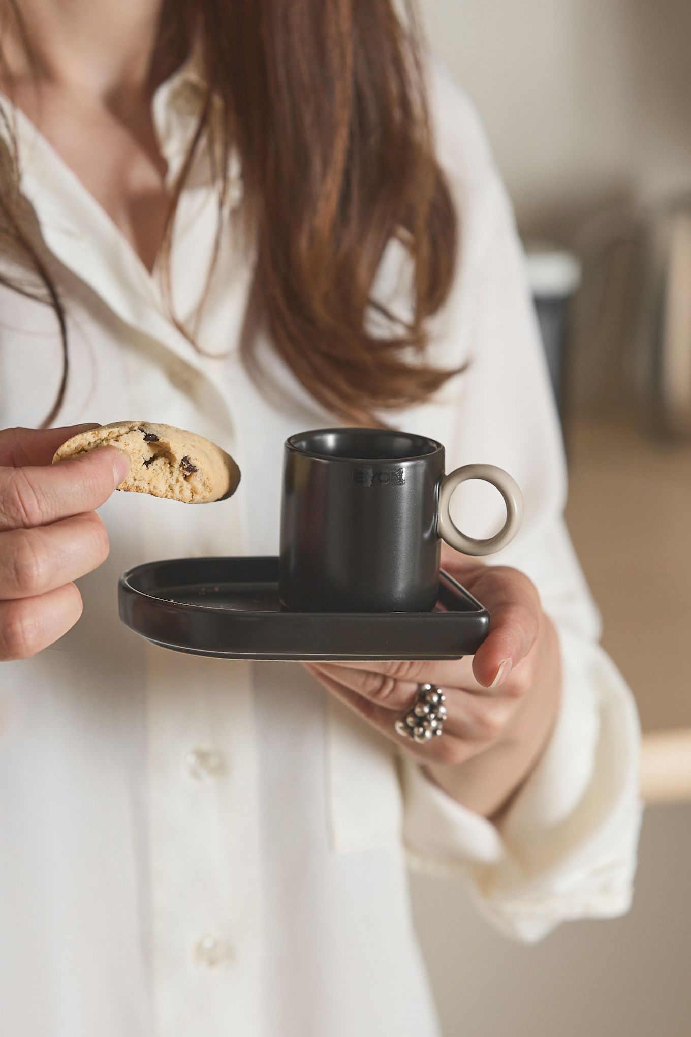 Aquí puedes ver a una mujer sosteniendo con una mano la taza de espresso Niki de Byon y con la otra un biscotti.