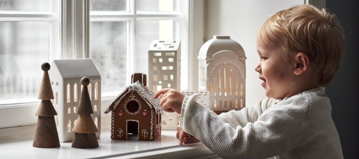 Cómo decorar con adornos navideños tradicionales escandinavos: un niño pequeño con una casa de jengibre, rodeado de portavelas en el estilo de un pueblo de jengibre.