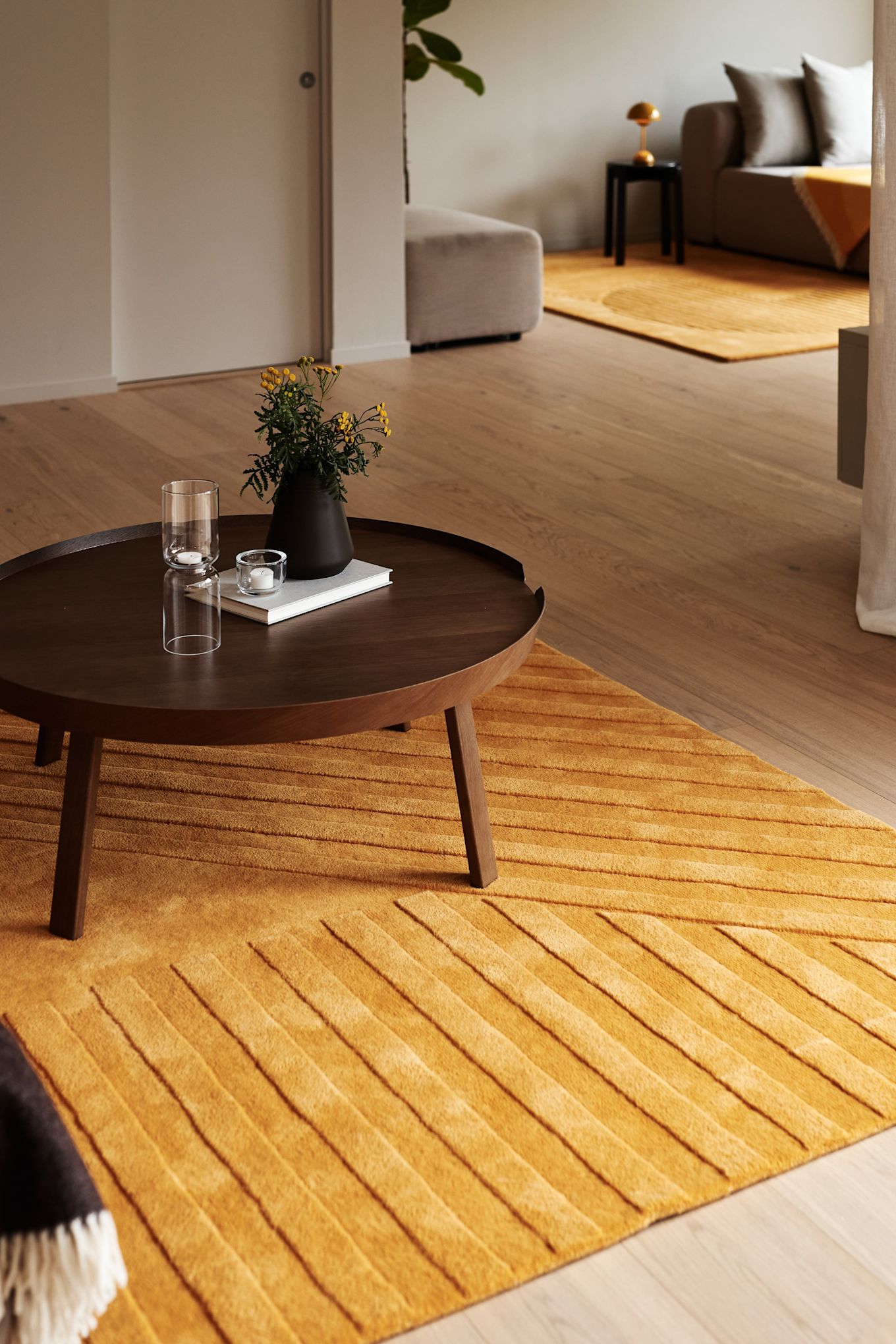 Alfombra para el salón: la alfombra de lana Levels Stripes en amarillo de NJRD está colocada en un salón armonioso con una mesa auxiliar de madera en tono marrón oscuro.