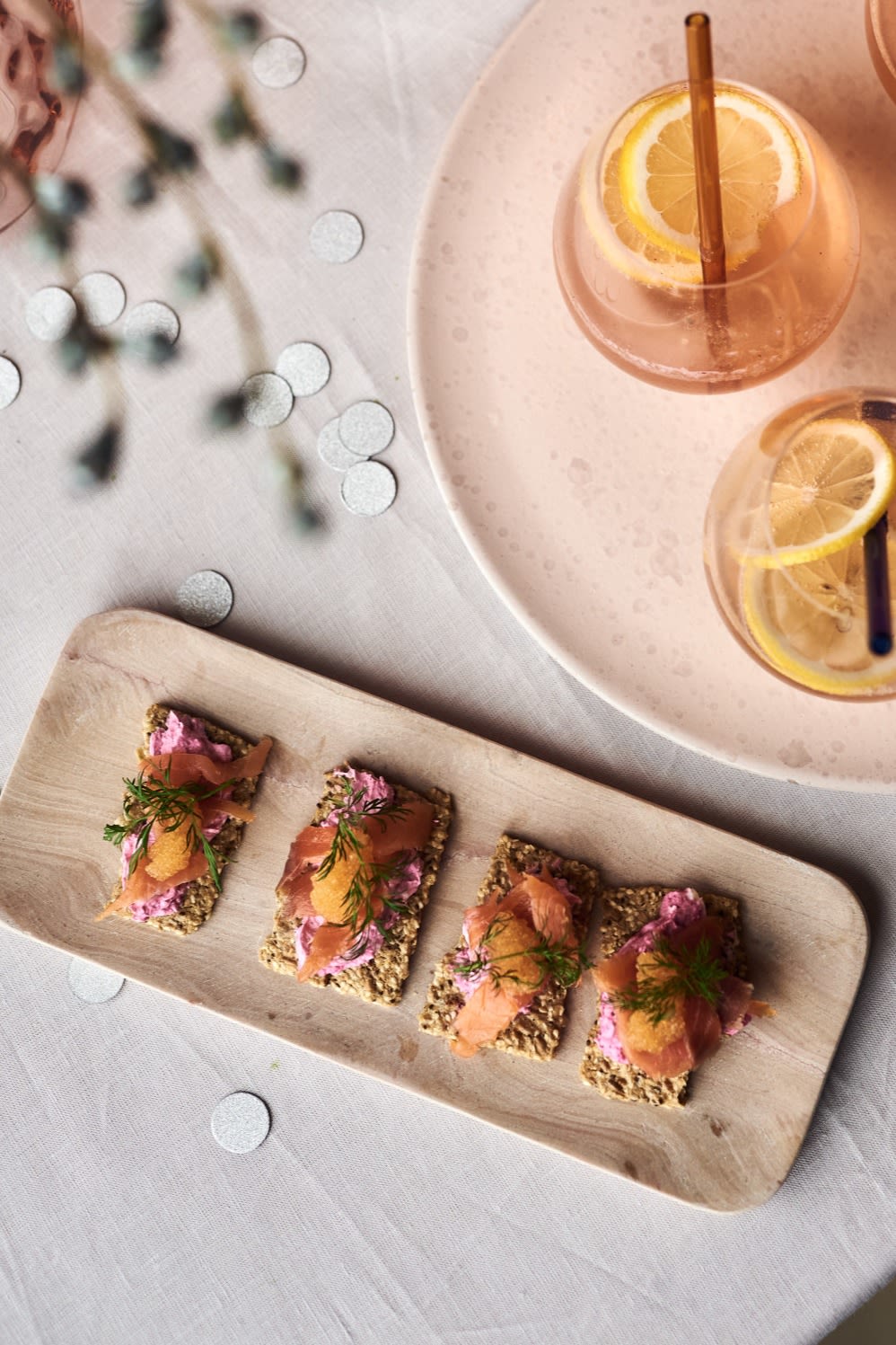 Canapés de salmón y remolacha, una de las recetas sencillas de entrantes para tu fiesta de Año Nuevo en la bandeja de mármol rosa de HK Living junto a un cóctel de champán.