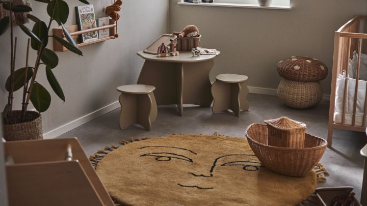 Colocar una alfombra grande y suave en el centro de la habitación crea una zona de juego acogedora y amplia a la hora de decorar la habitación infantil. Aquí la alfombra con forma de sol Sun de Ferm Living en una habitación infantil con mesa, taburetes y cuna.