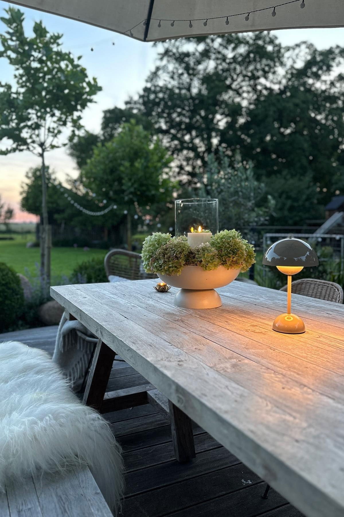 Una terraza acogedora con una gran mesa de comedor y bancos, decorada con velas y una lámpara de mesa Flowerpot de &Tradition.