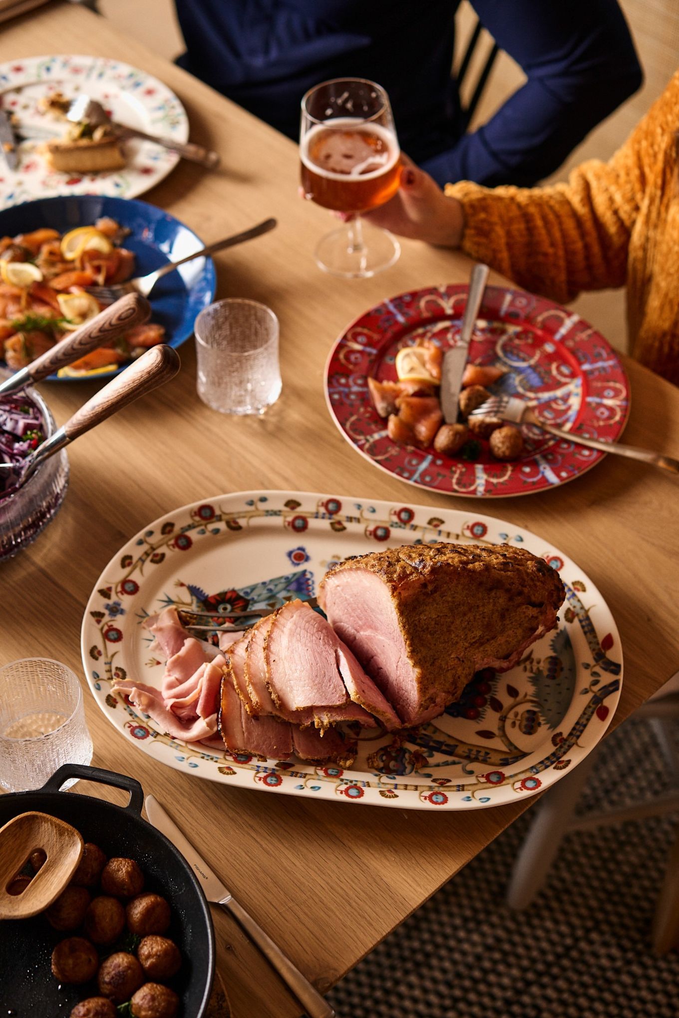 Una pierna de jamón en rodajas se presenta en una mesa navideña nórdica tradicional.