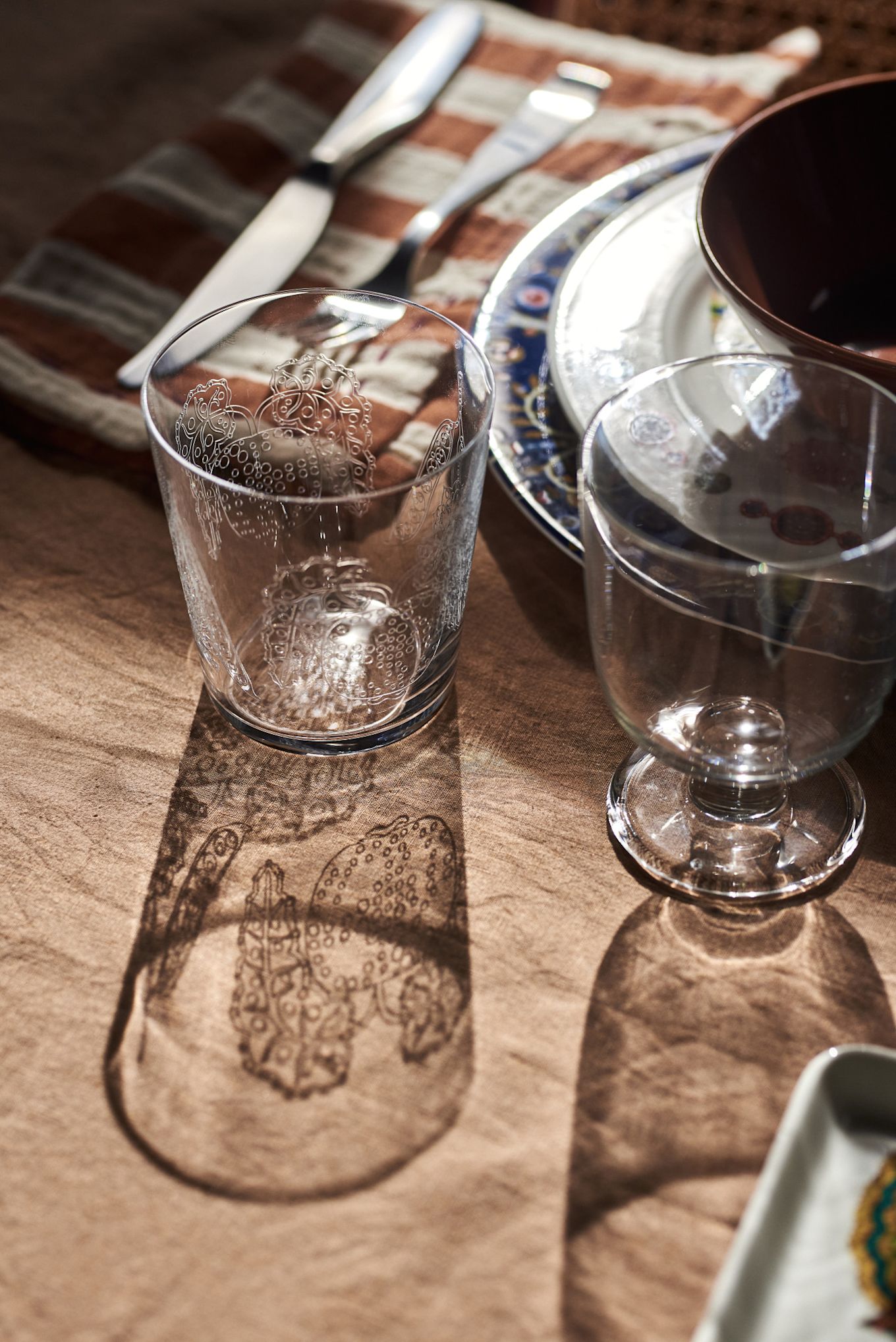 El sol brilla a través del vaso de bebida Taika, proyectando una sombra sobre la mesa en una idea de decoración de mesa bohemia.