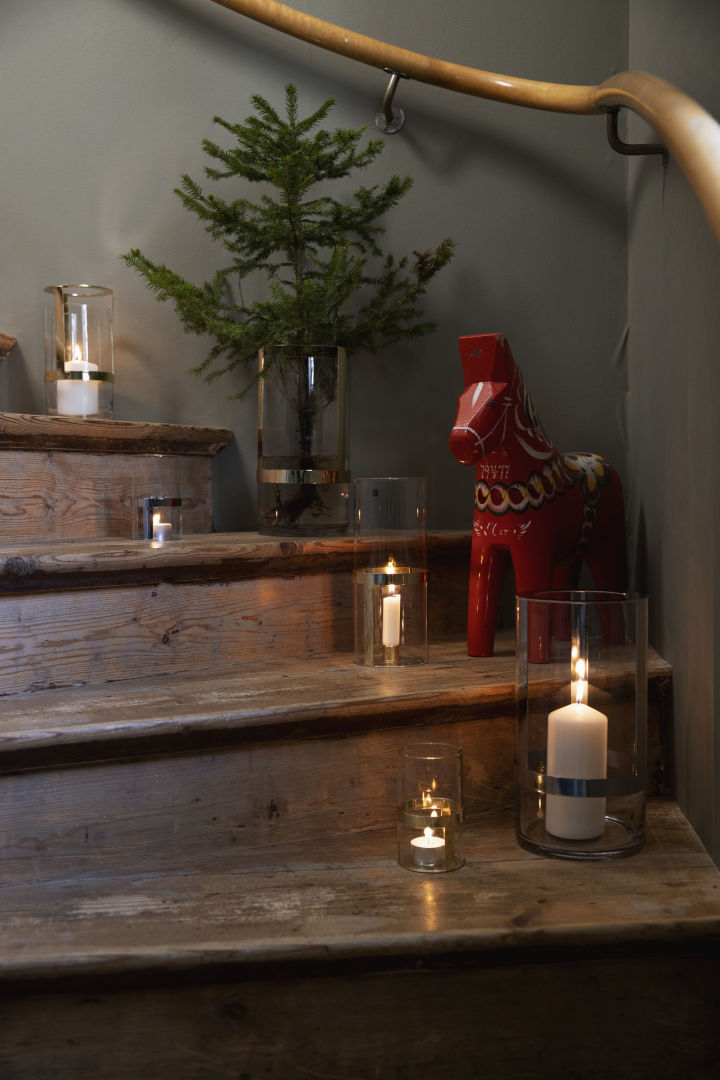 Decora también la escalera para entrar en el ambiente navideño. Coloca la jarrón Hold de Sagaform en diferentes tamaños en varios escalones y llénalos con velas y ramas de abeto. Un caballo Dala completa la decoración.