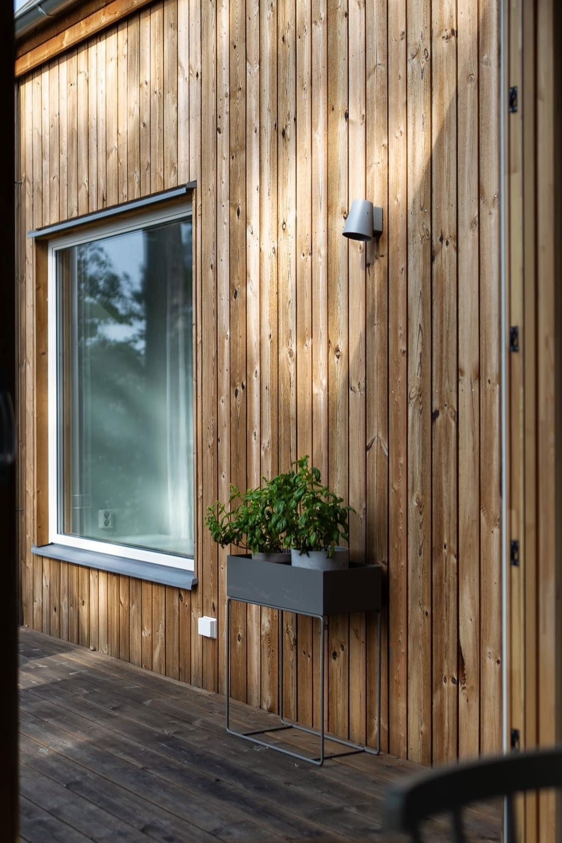 Aquí puedes ver la Plant Box de metal en negro de Ferm Living en la terraza de una casa de madera sueca.