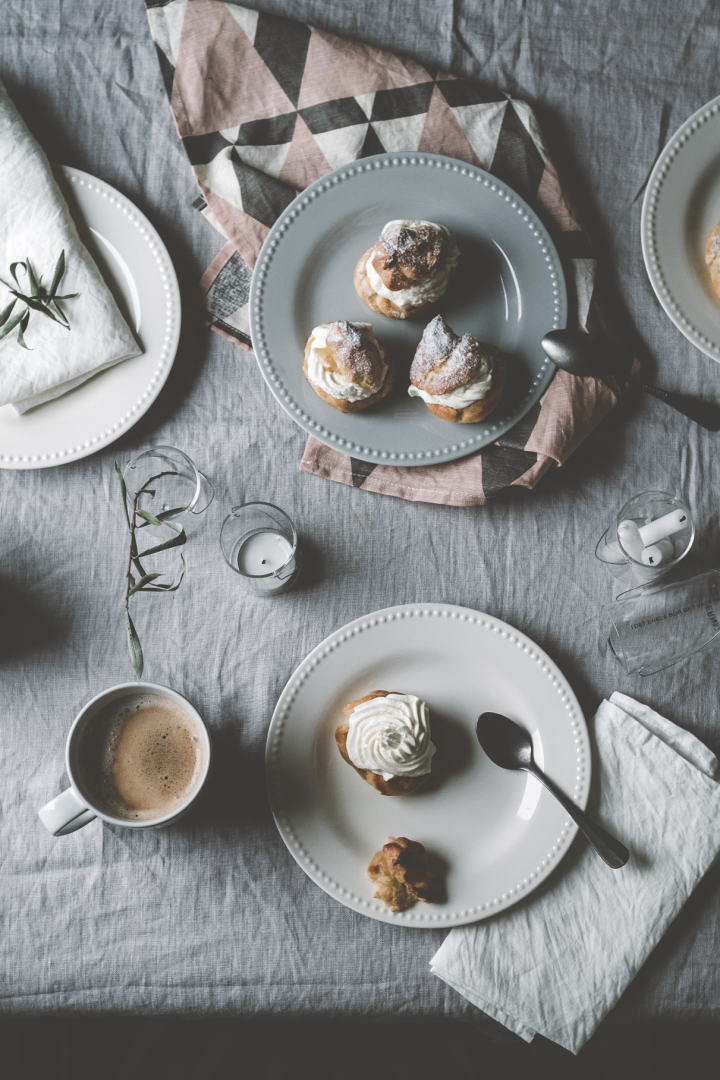 Aquí puedes ver los semlor de @kohlundkimchi en una mesa, sobre platos de diferentes colores de la colección Dots de Scandi Living, acompañados de una taza de café.