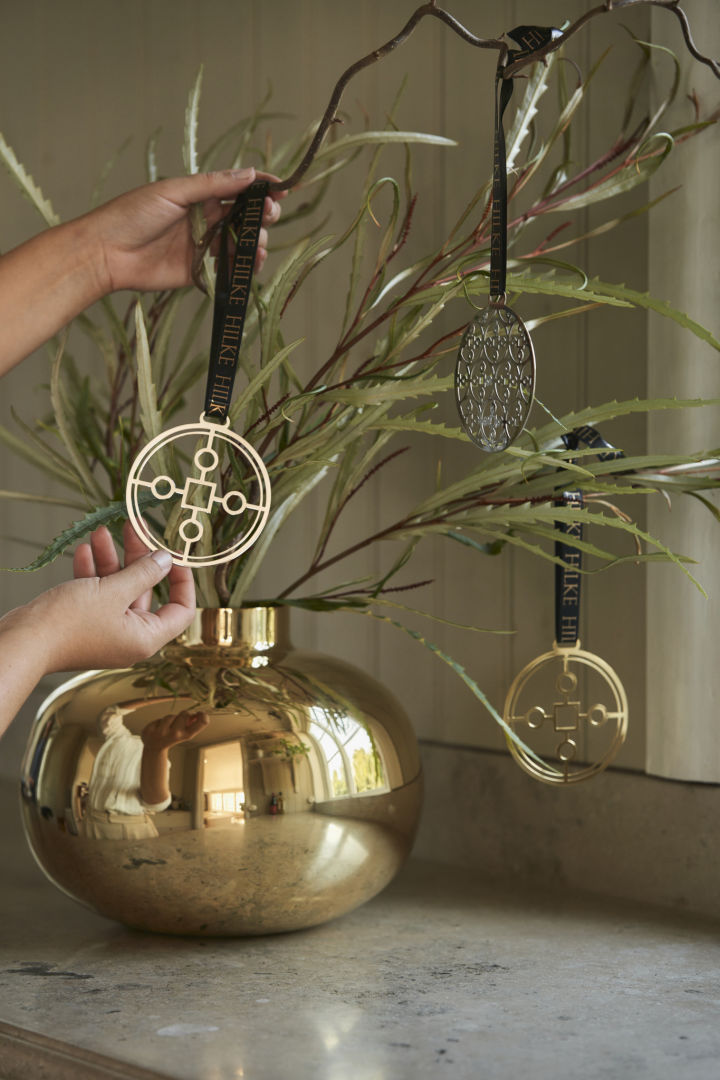 Para decorar tu mesa de manera hermosa, puedes colocar algunas ramas en el jarrón Amico de color dorado y decorarlas con la decoración de árbol Anima Gemella.