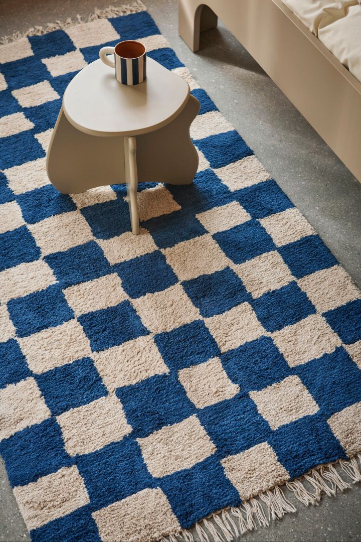 Una alfombra estampada como la Mara de cuadros en azul y blanco de Ferm Living se convierte en un detalle suave y decorativo en la habitación infantil.