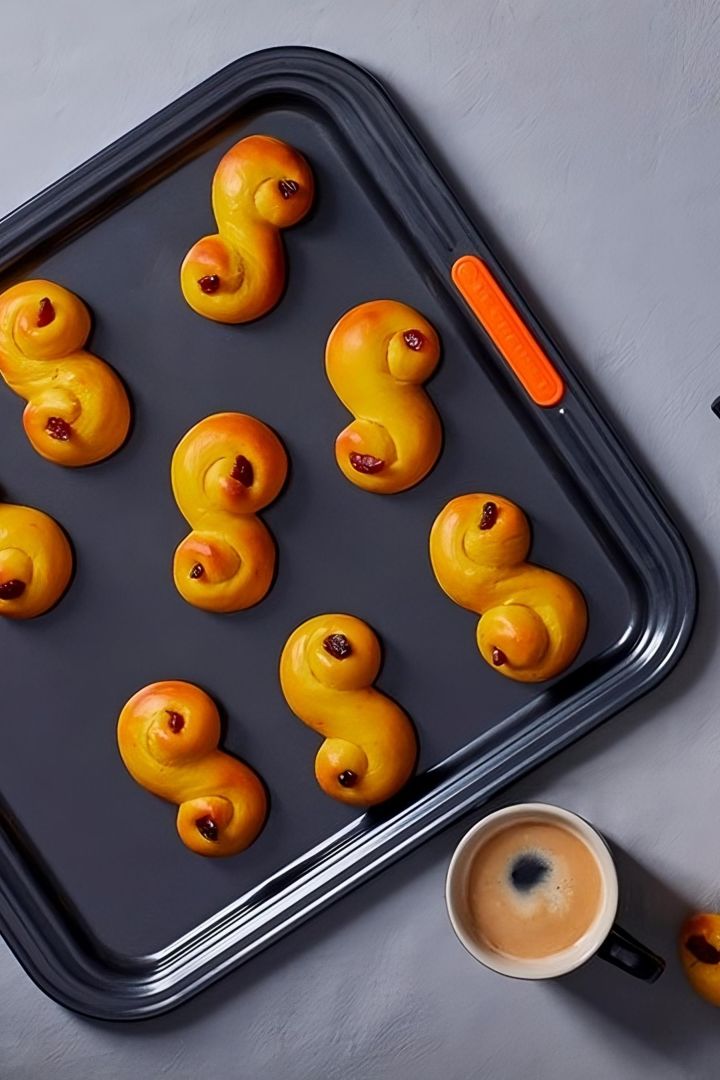 Los lussekatter son un pastel sueco especial que se consume principalmente en Navidad. Aquí puedes ver deliciosos lussekatter horneados, de un color dorado y marrón, en una bandeja de hornear de Le Creuset.