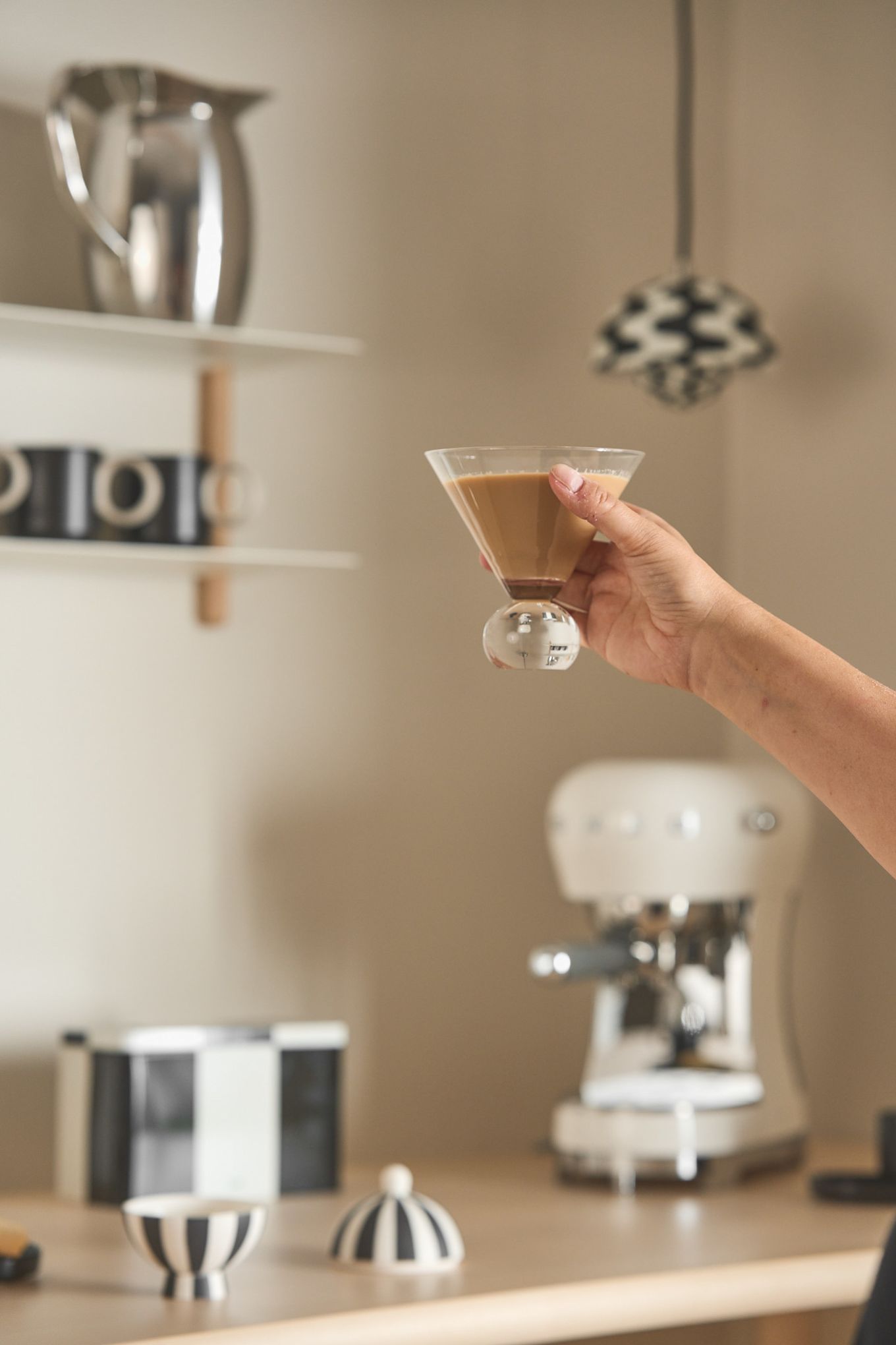 El rincón de café perfecto en casa incluye, por supuesto, los vasos adecuados. Aquí puedes ver una mano sosteniendo un vaso Spice de Byon lleno de café, con un rincón del café al fondo.